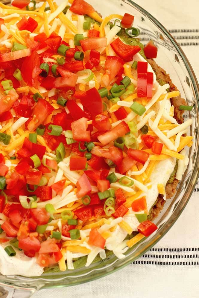 Cajun 7 Layer Dip - Layers of refried beans, black-eyed peas, guacamole, cajun sour cream, and Tony Chachere's Creole Seasoning topped with red bell peppers, tomatoes, green onions, and shredded cheese.