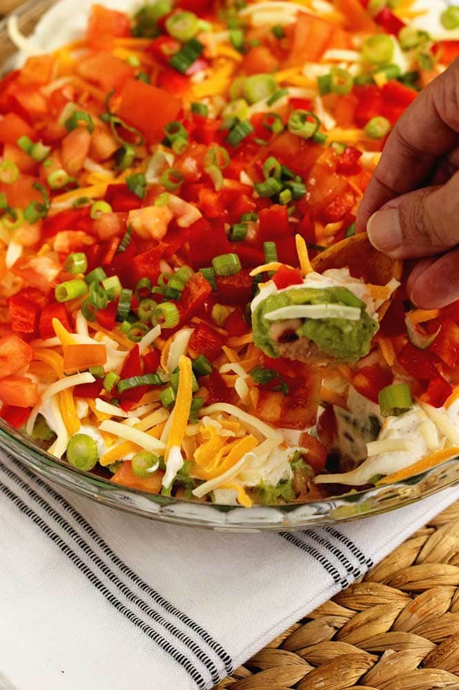 Cajun 7 Layer Dip - Layers of refried beans, black-eyed peas, guacamole, cajun sour cream, and Tony Chachere's Creole Seasoning topped with red bell peppers, tomatoes, green onions, and shredded cheese.