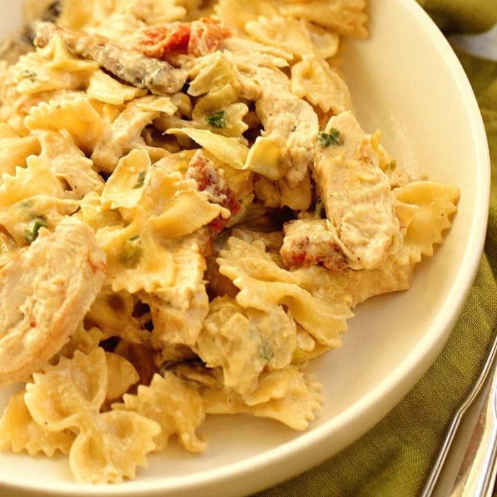 Copycat Spicy Romano Chicken Pasta - Make this creamy restaurant-style chicken pasta made with bow-tie noodles, sun-dried tomatoes, artichoke hearts, mushrooms, and grilled chicken tossed in a creamy dreamy sauce.